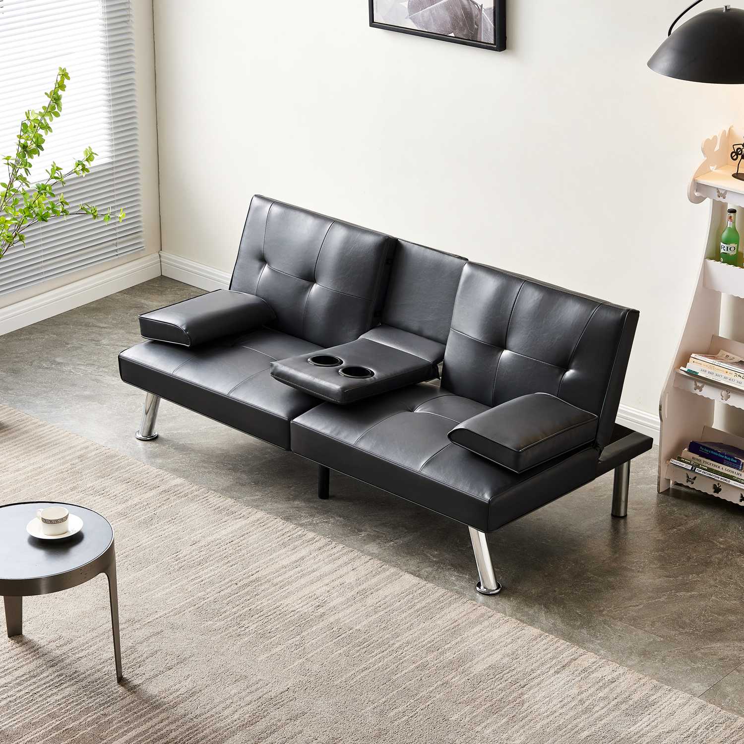 Black faux leather sofa bed in a living room setting with a coffee table and decorative items.