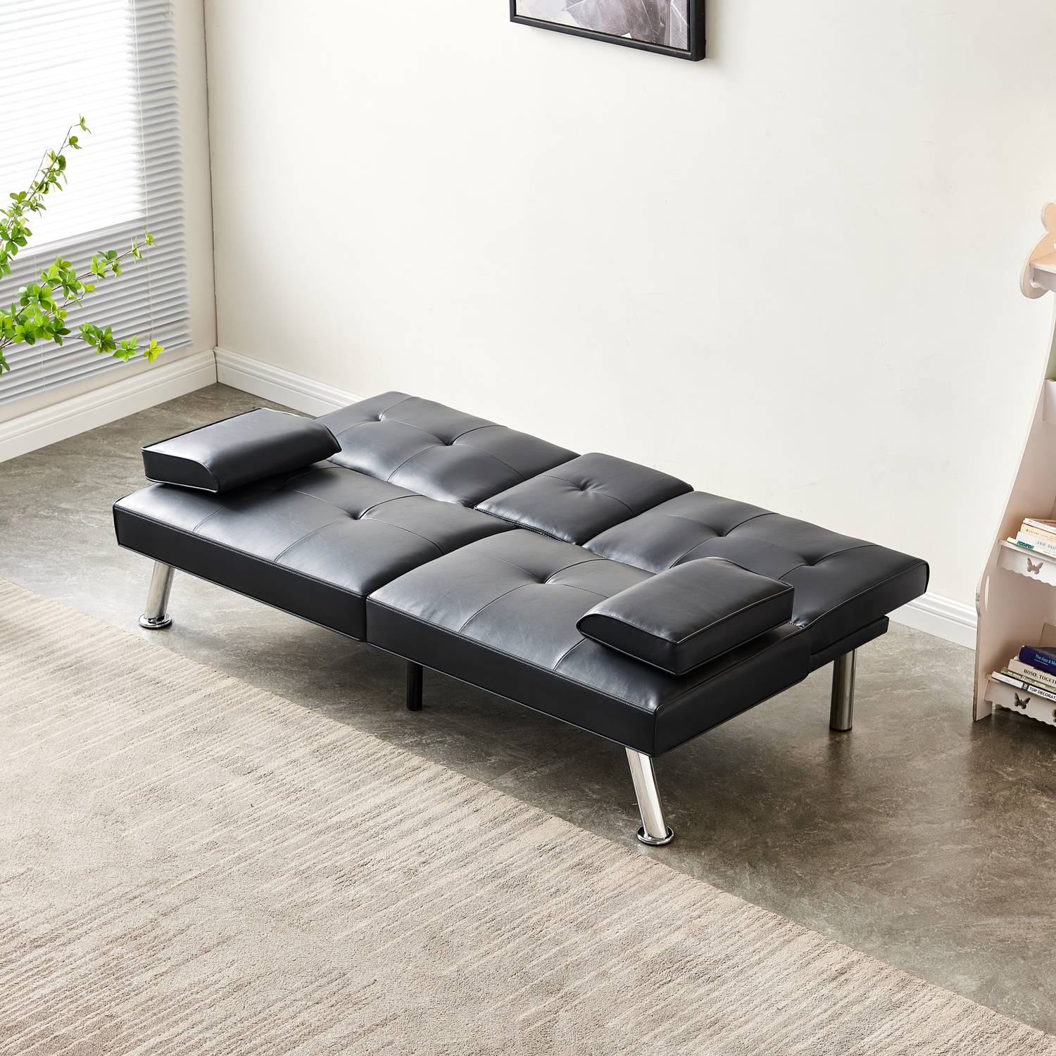 Black faux leather sofa bed in a room with a window and plant.