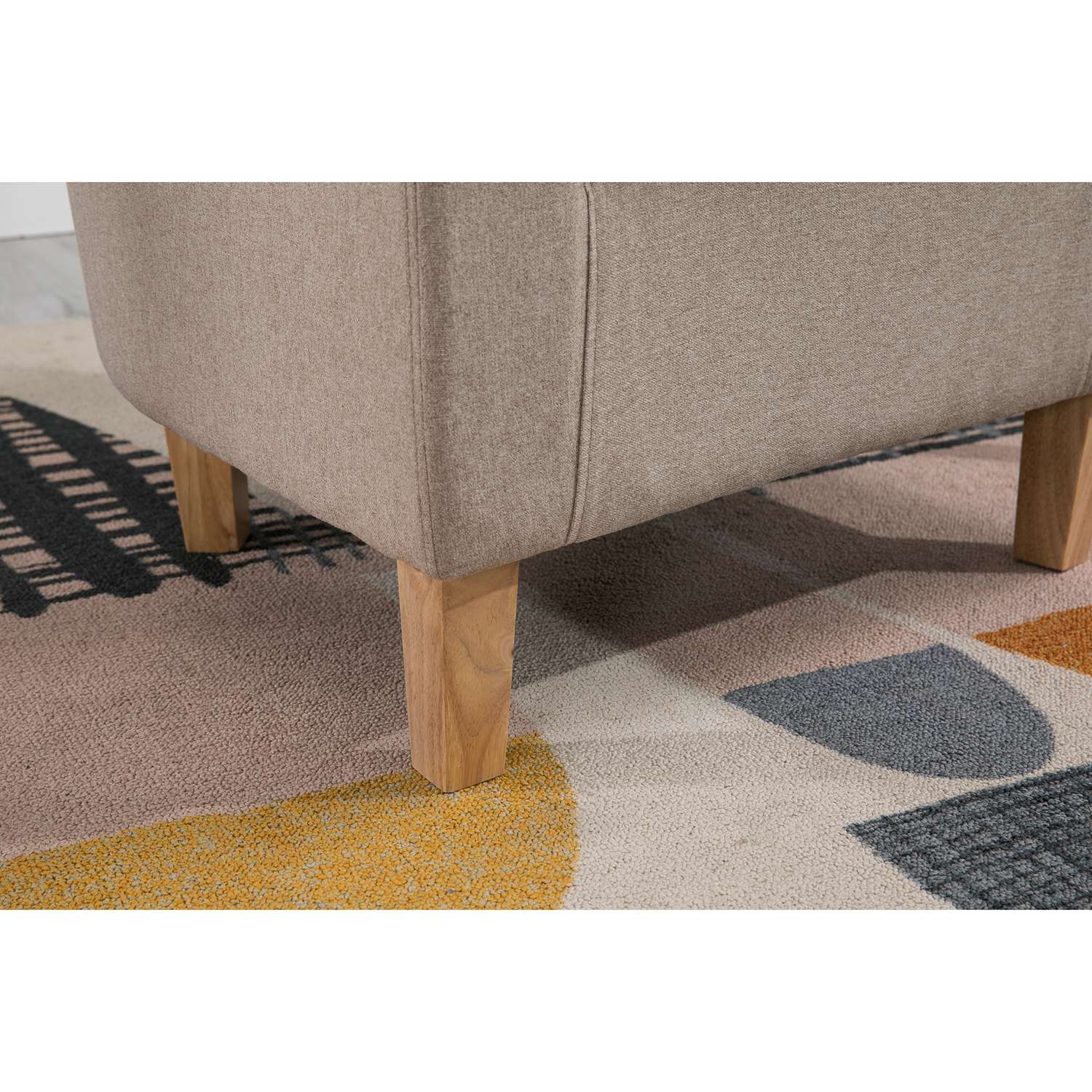 Close-up of a cream tub chair with wooden legs on a patterned rug.