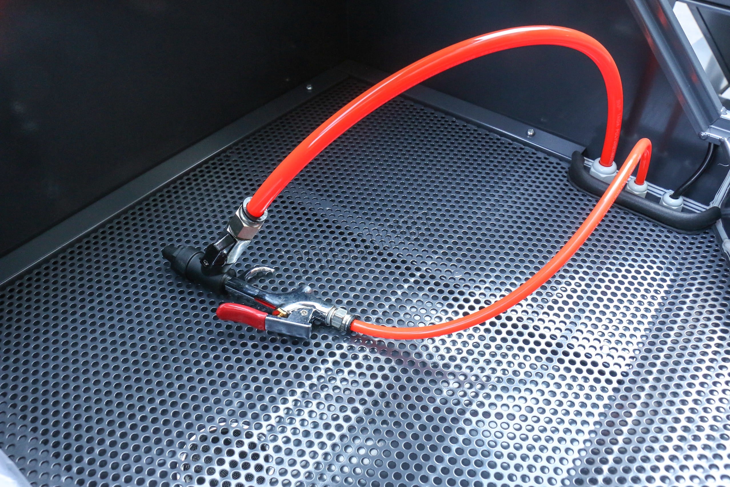 Red and black jump starter cable in an industrial parts washer.