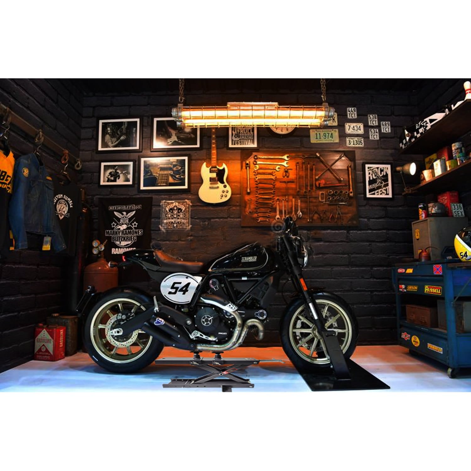 Motorcycle on a motorbike scissor lift in a garage setting with tools and decor on the wall.