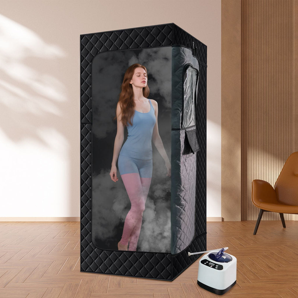 Woman standing inside a black portable sauna tent with a small white device on the floor.