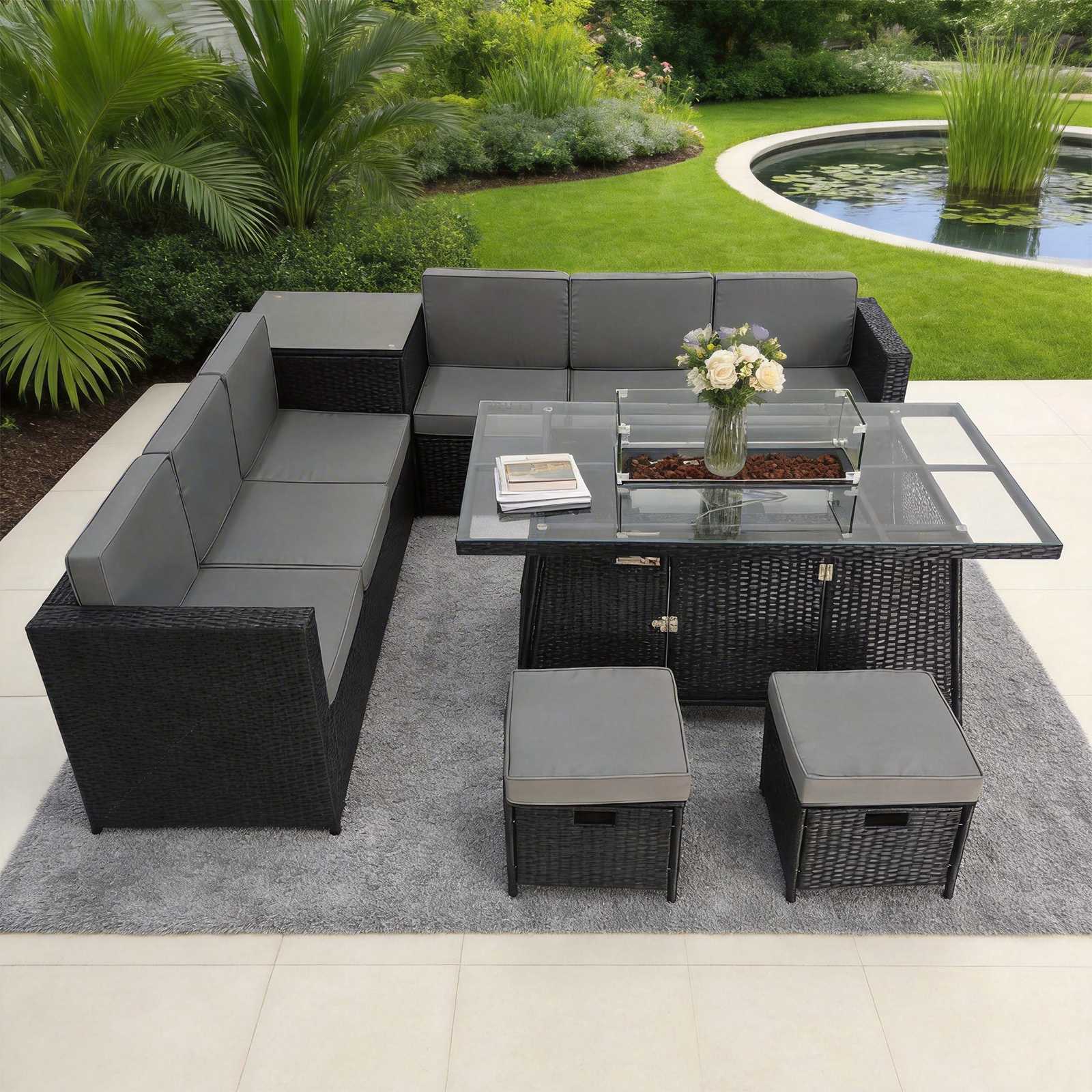 outdoor rattan dining set with a glass fire pit table with flowers on a patio with a garden background.