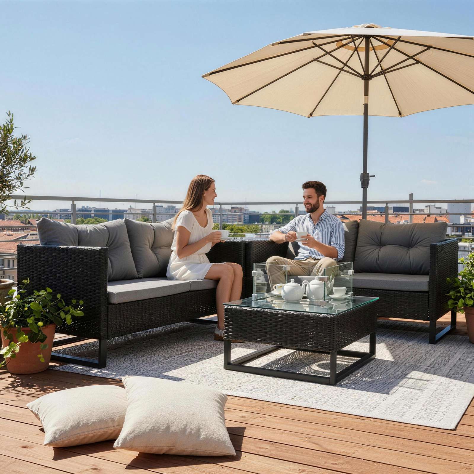 Image of two people seating on a rattan furniture set with an outdoor fire pit table with a city skyline on the background. 