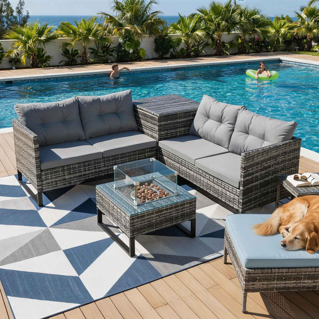 image of a rattan furniture set with a central outdoor fire pit table on a patio flooring with a pool in the background.