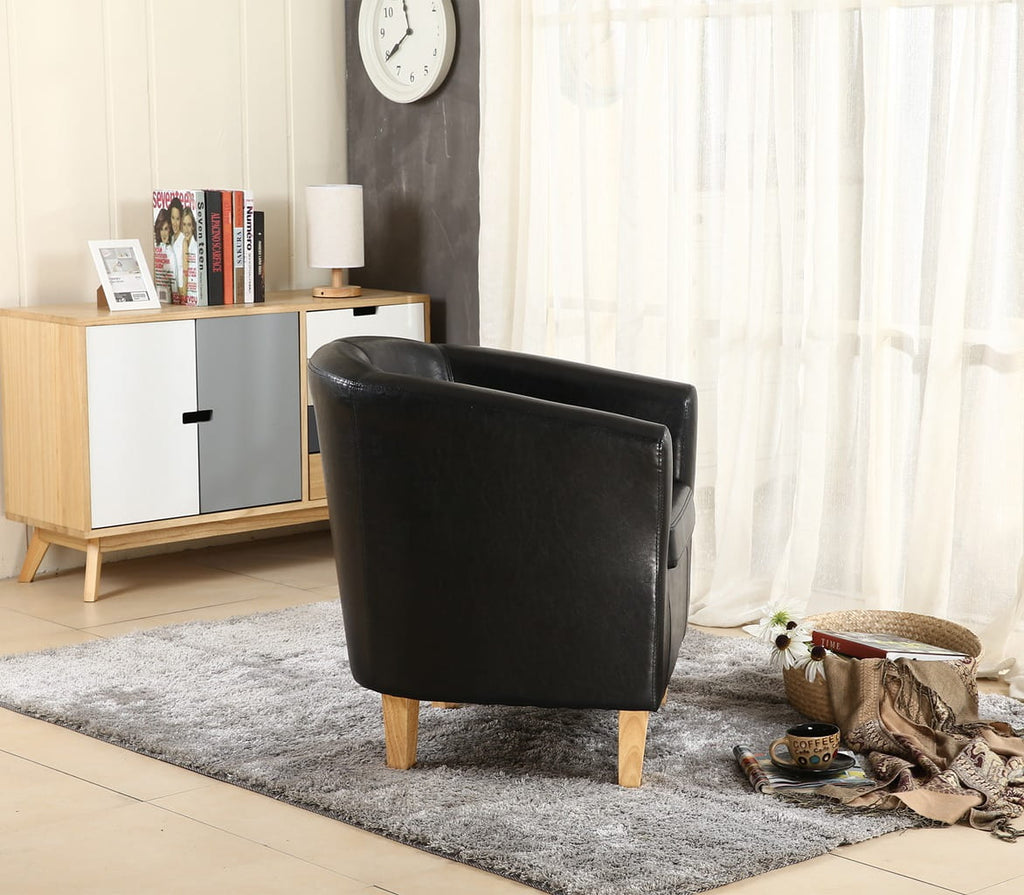 Black faux leather armchair in a living room setting with a wooden cabinet and decorative items.