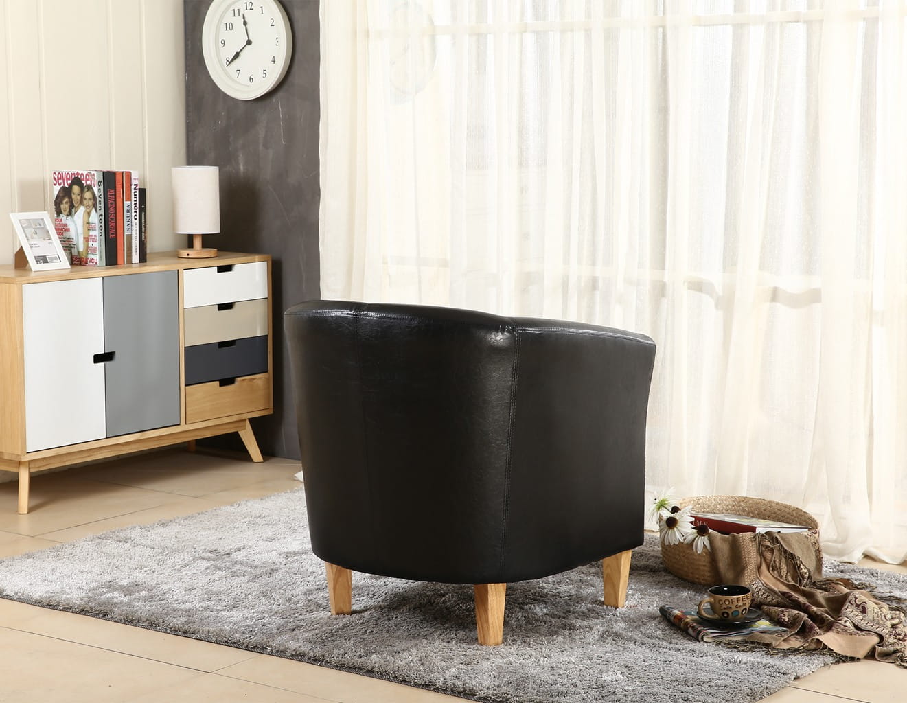 Black faux leather armchair in a room with a sideboard and window curtains.