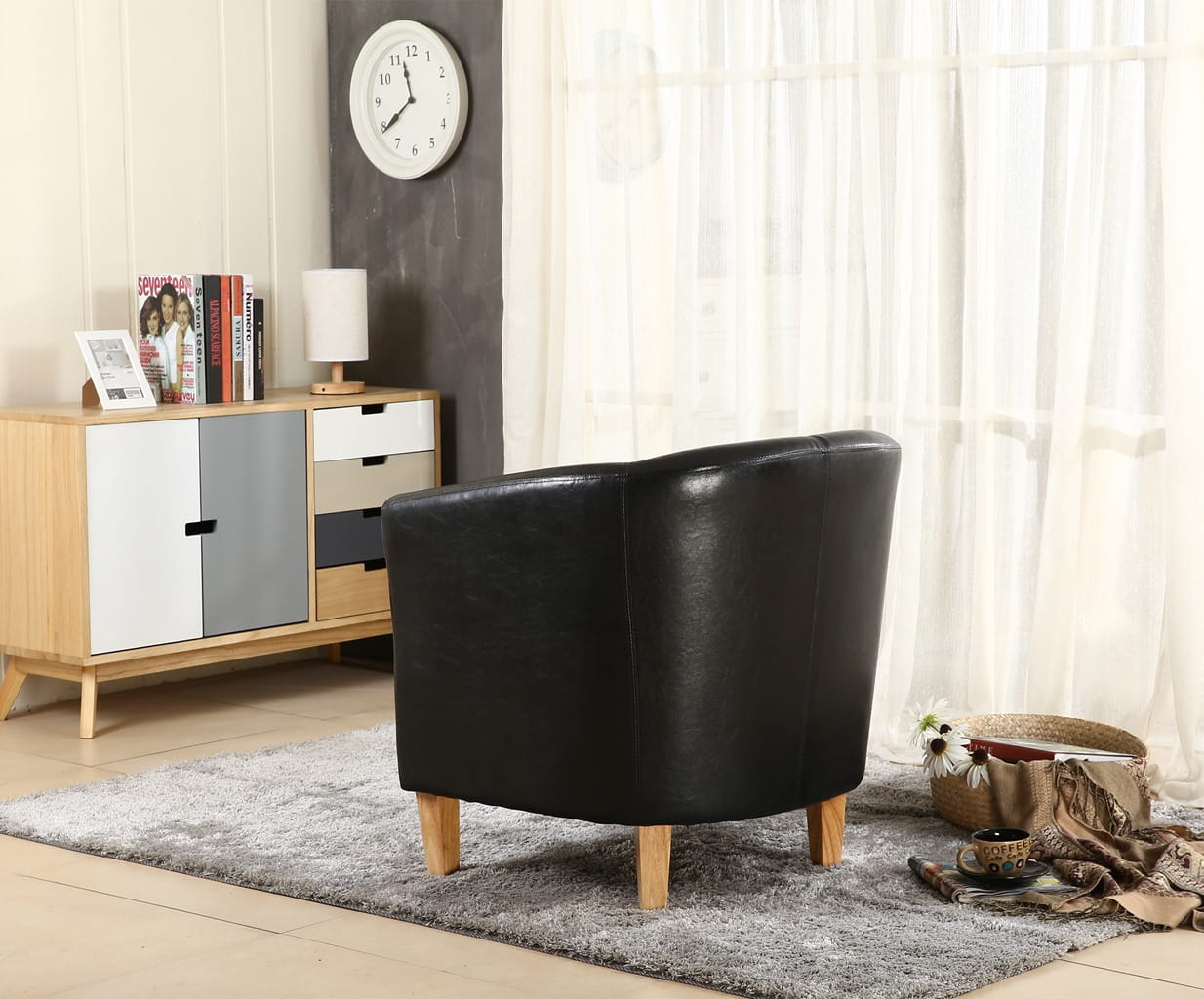 Black faux leather armchair in a living room with a wooden sideboard and clock on the wall.
