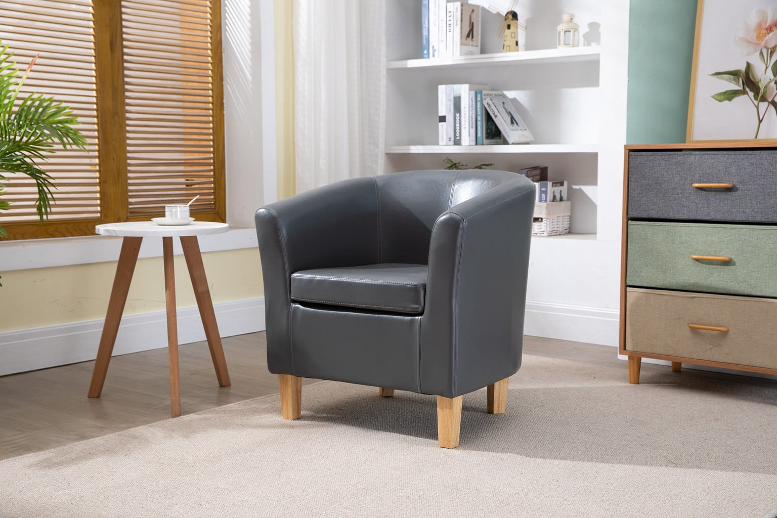 Grey faux leather armchair in a room with a small table, bookshelf, and dresser.