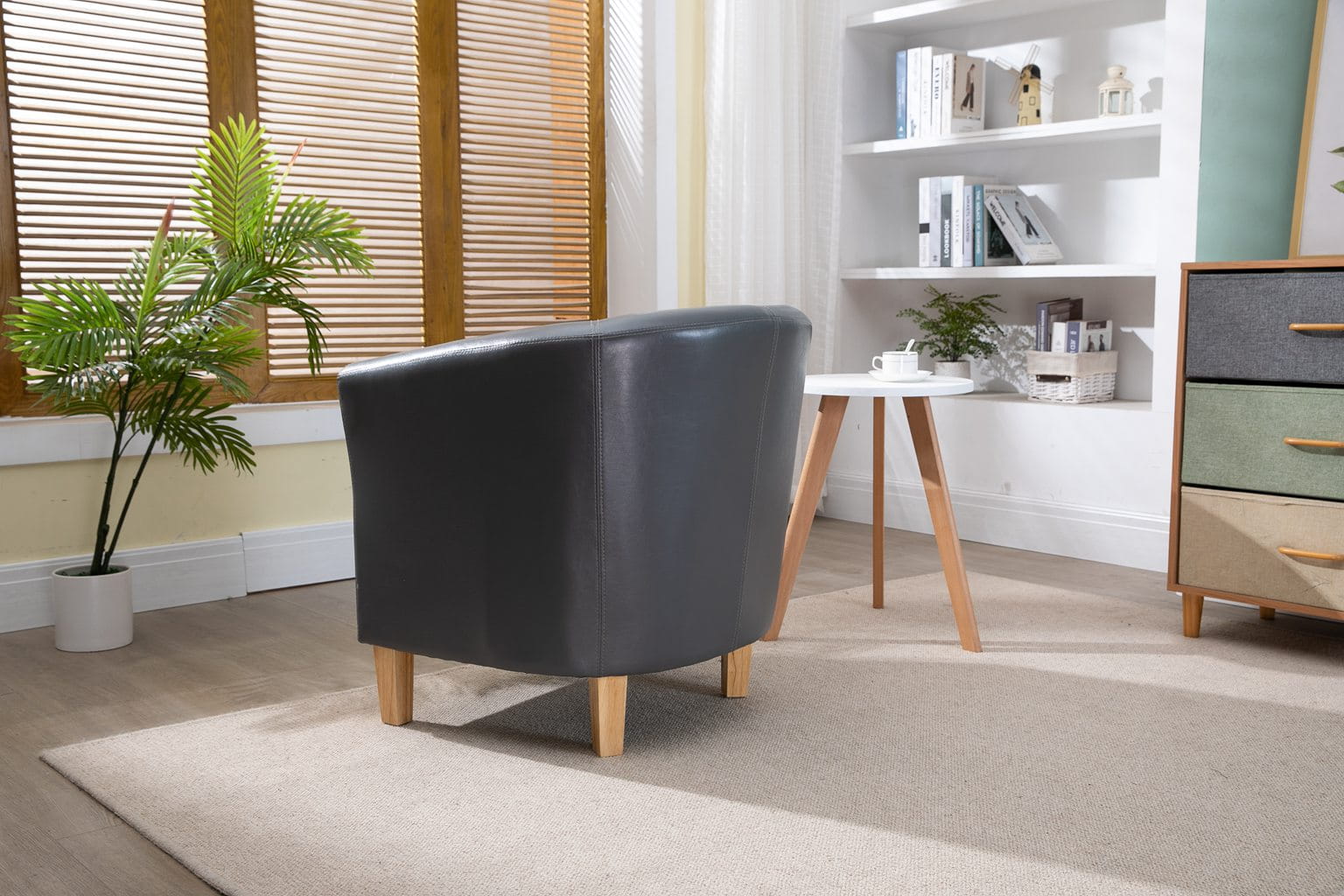 Modern living room with a faux leather grey armchair, white bookshelf, and wooden floor.