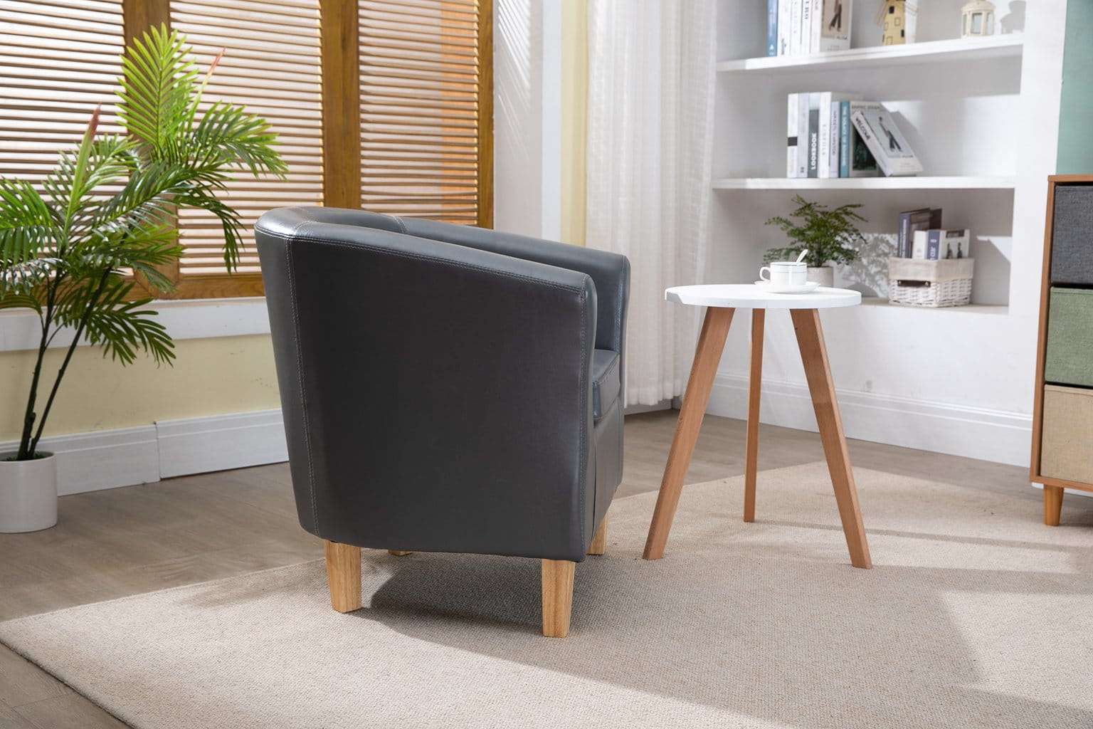 Grey faux leather armchair in a living room with a small table and bookshelf.
