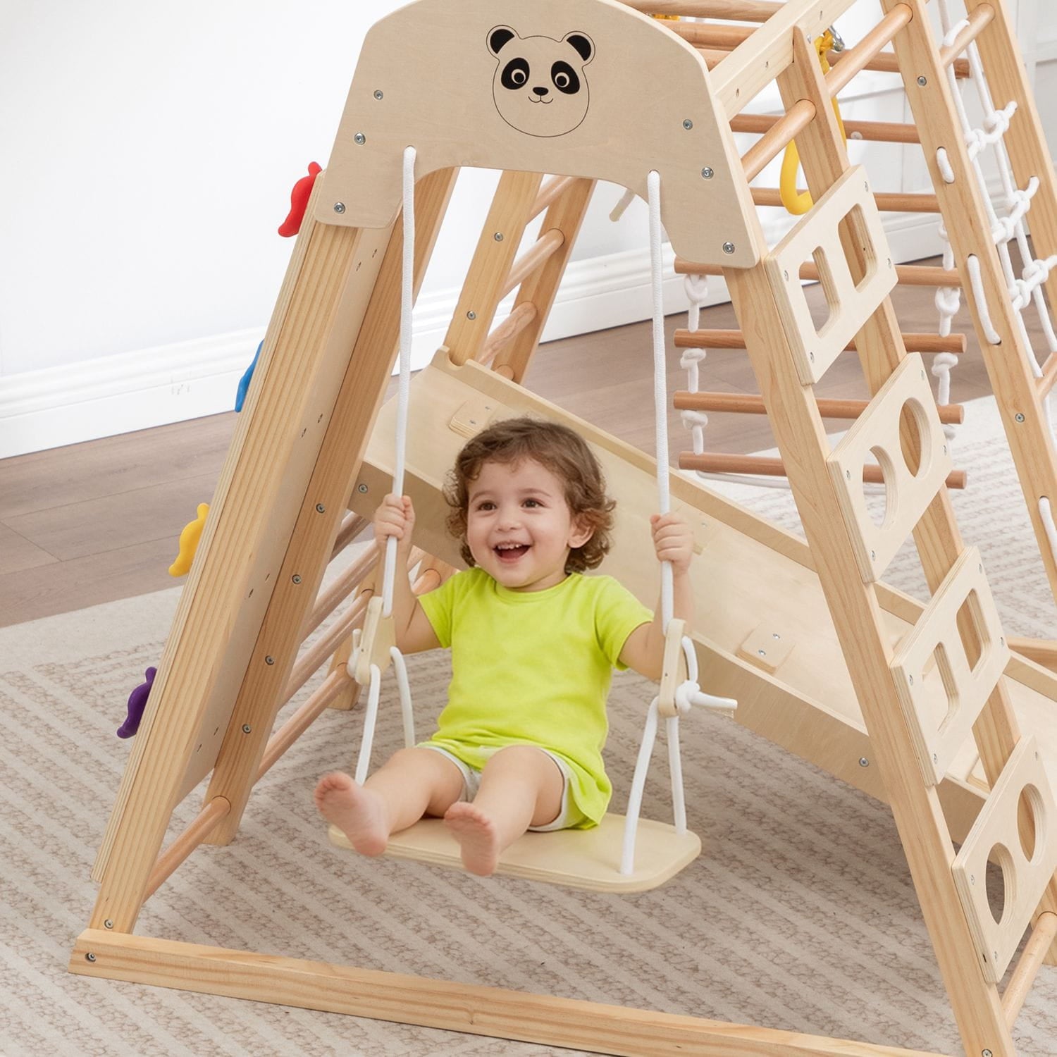 Child on a wooden swing set with a panda design, from a wooden climbing frame, smiling.