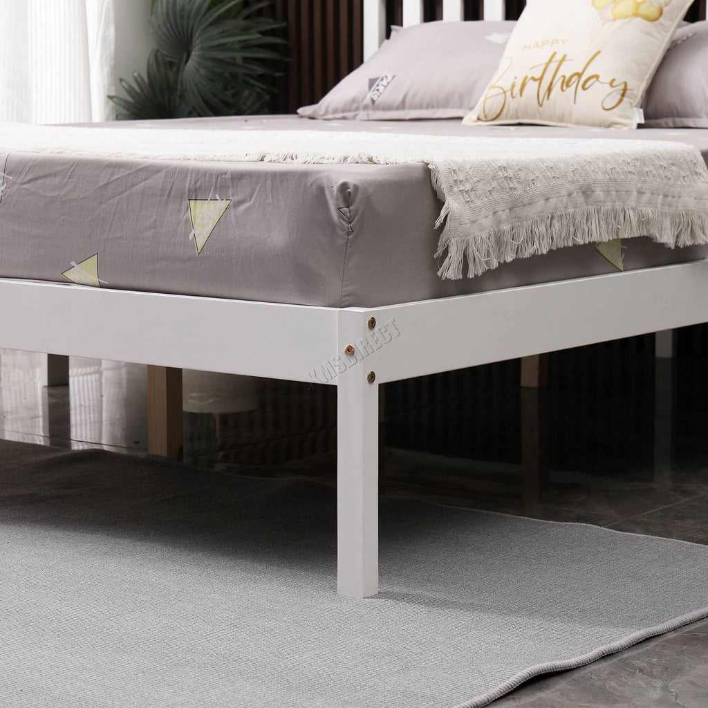 White wooden double bed frame with grey mattress and decorative pillows in a room setting.