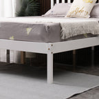 White wooden double bed frame with grey mattress and decorative pillows in a room setting.