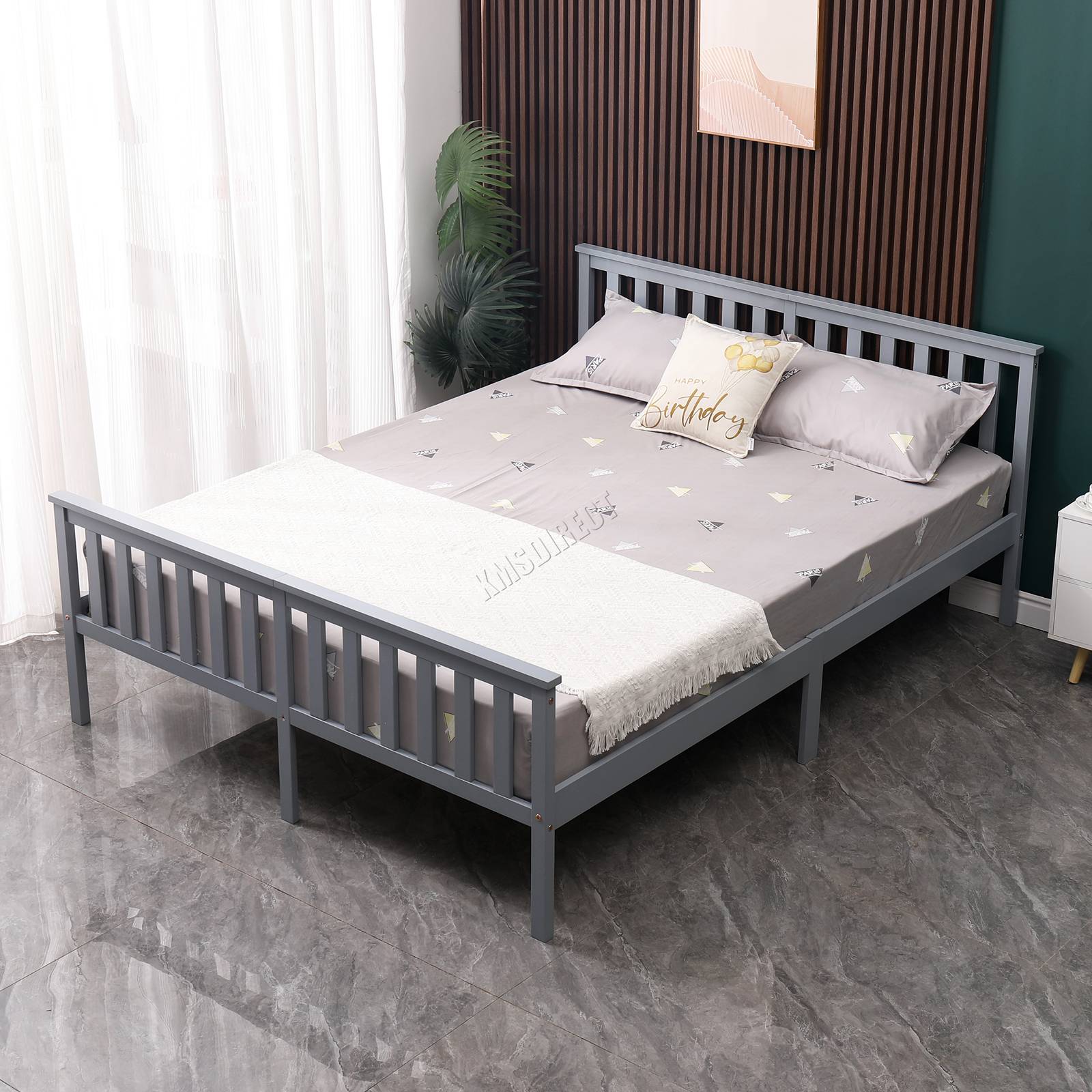 Grey wooden double bed frame with bedding in a room with white curtains and a plant.