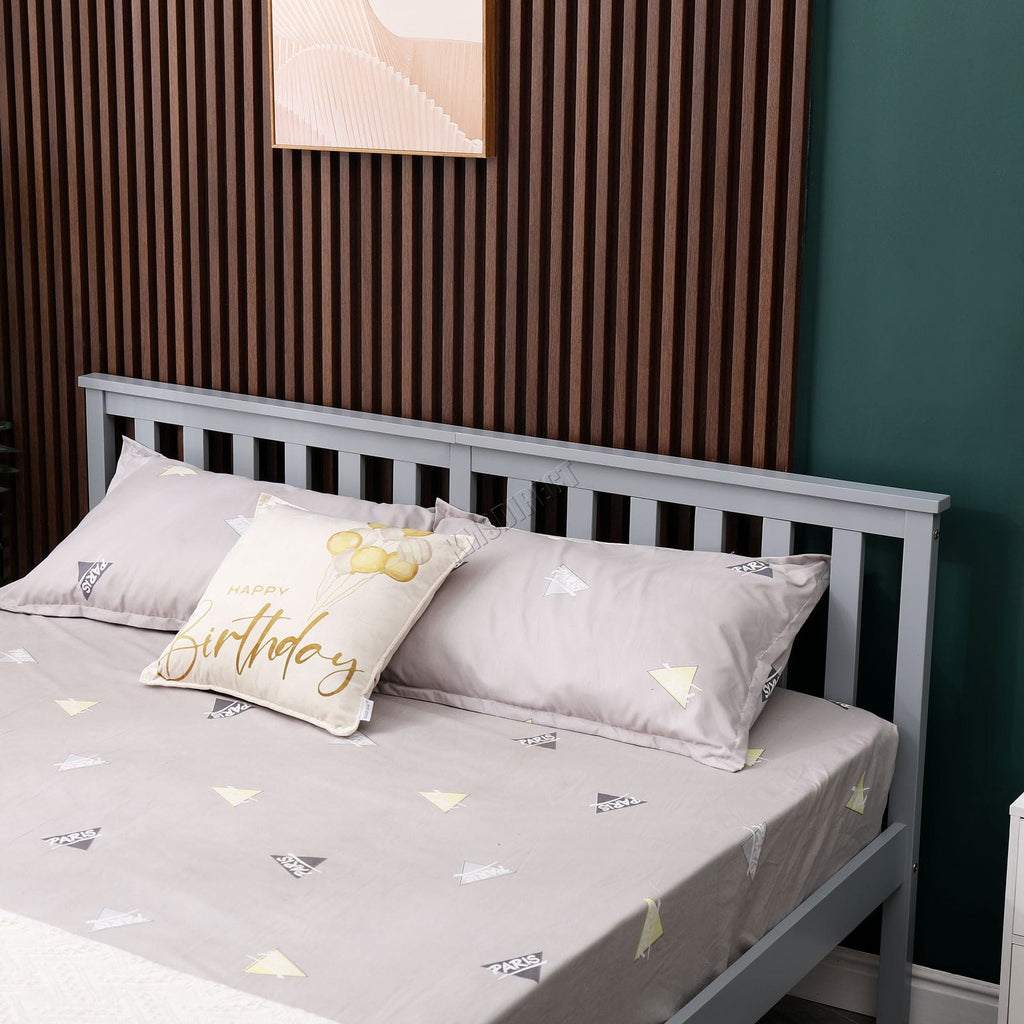 Wooden double bed with grey bedding and decorative pillows against a wooden headboard and green wall.