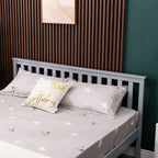 Wooden double bed with grey bedding and decorative pillows against a wooden headboard and green wall.