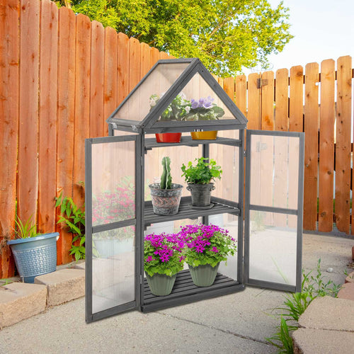 Portable wooden greenhouse with plants against a wooden fence